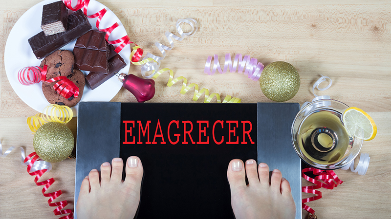 Pessoa a pesar-se numa balança onde aparece a palavra emagrecer, com um prato de doces ao lado